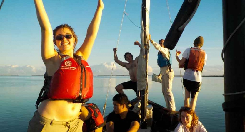 a group of students raise their hands in success on a sailboat in florida